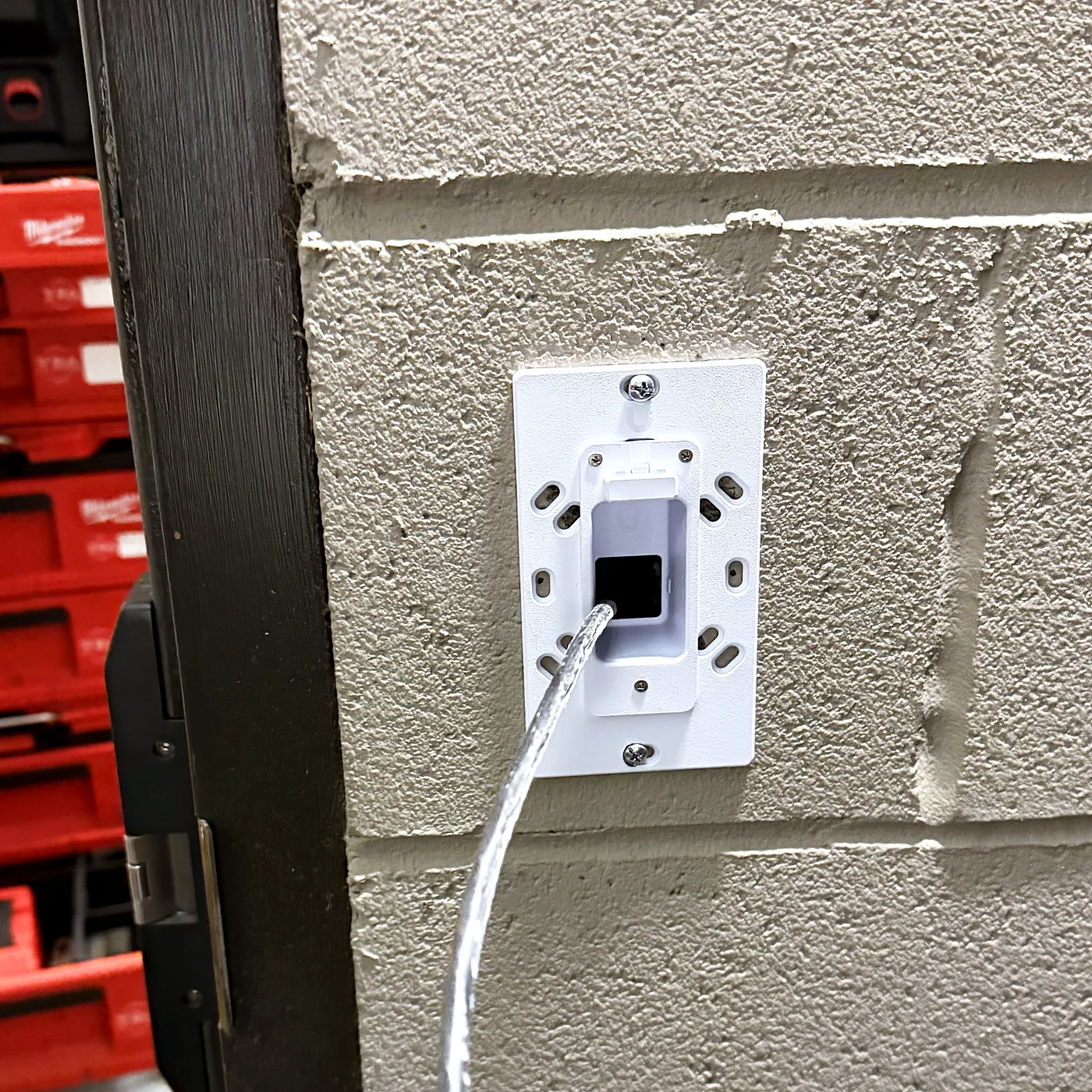 A single data outlet in a white plate mounted on a painted block wall, with a patch cord plugged in and tool cases stacked behind.