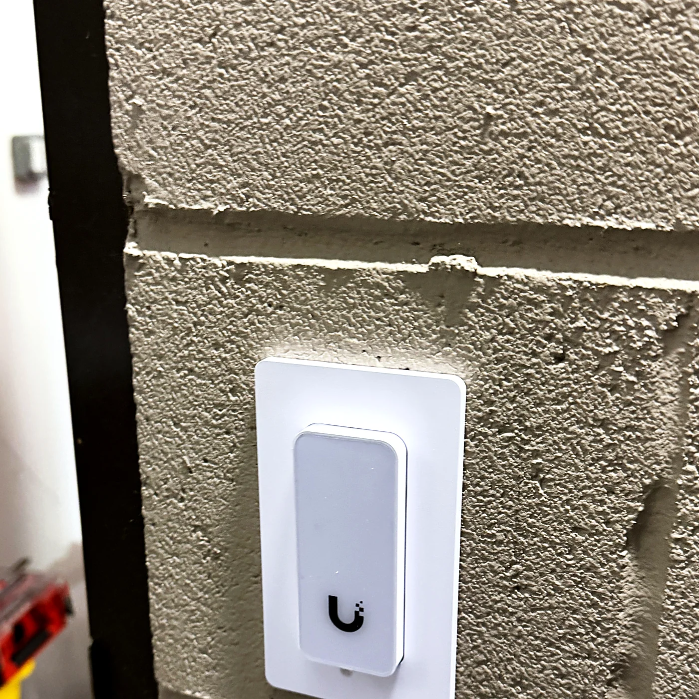 An access control reader mounted on a painted block wall, with tool cases still on the floor below.