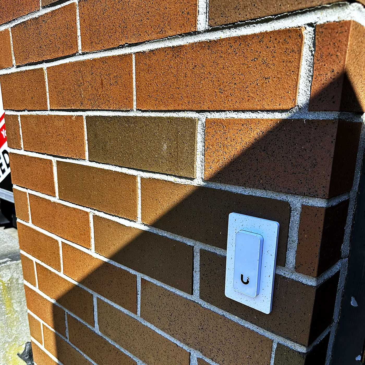 An access control reader mounted flush against a brick wall in raking afternoon light.