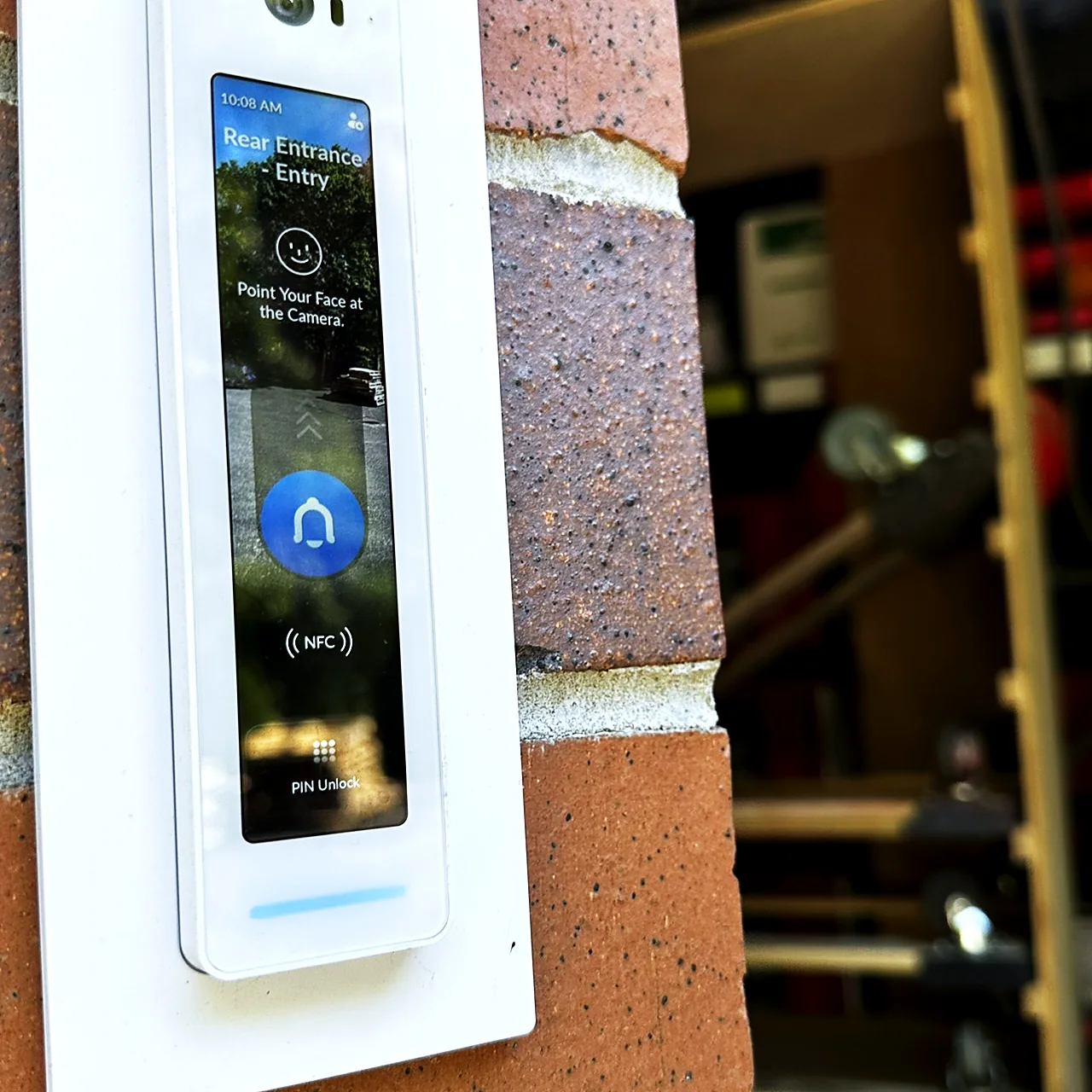 A touchscreen door intercom mounted on a brick pier at the entrance to a working yard.