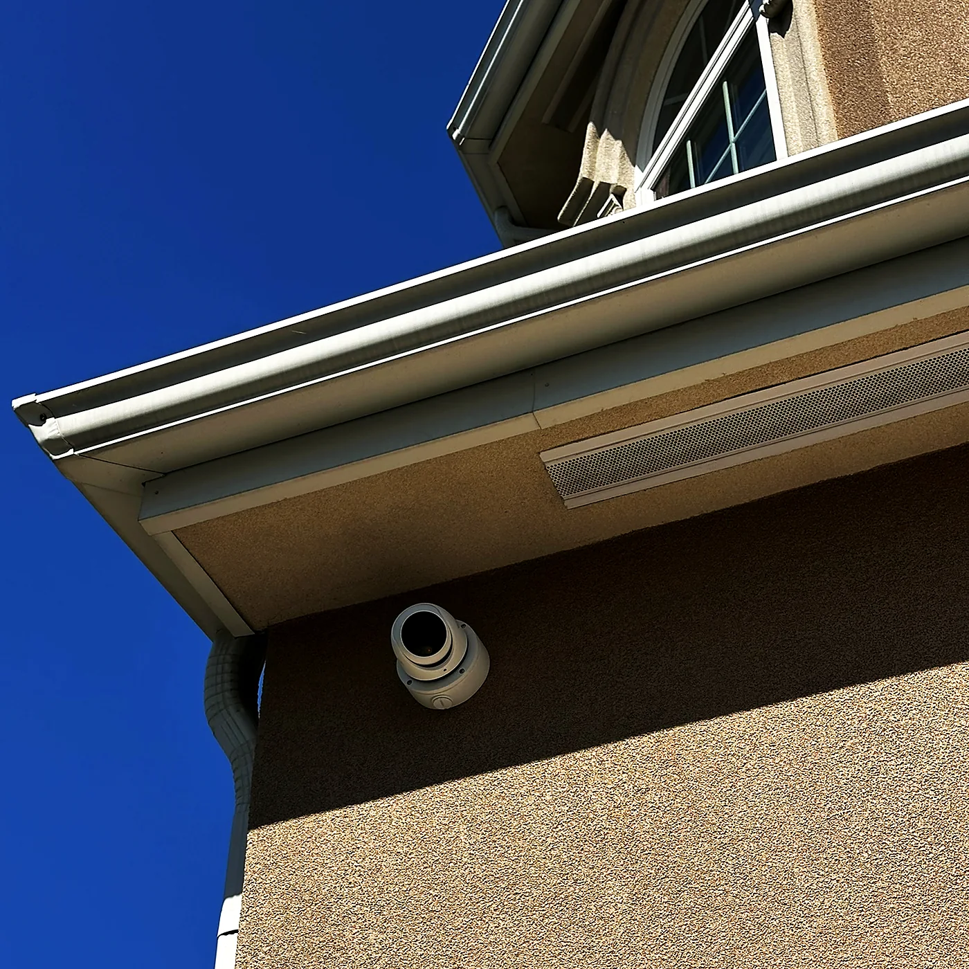 A camera mounted under a building soffit against a deep blue sky, with the cable run concealed behind the fascia.
