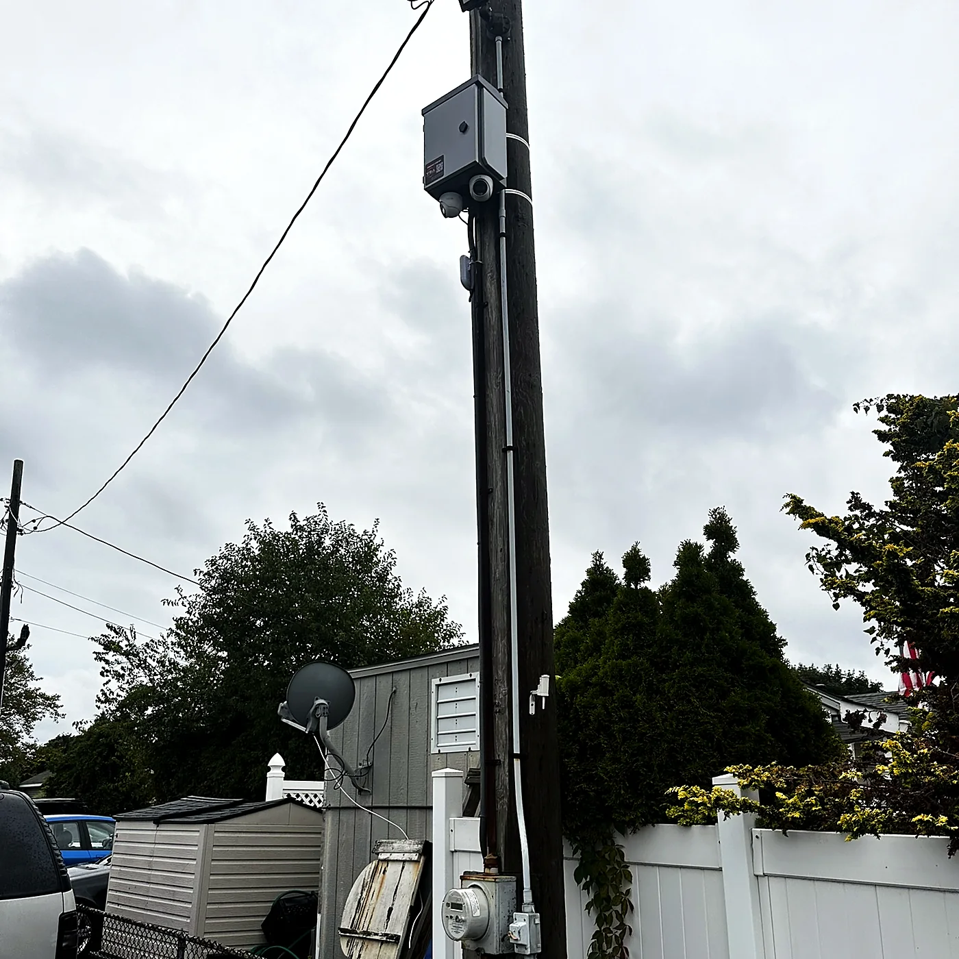 A camera and equipment enclosure mounted on a pole above a fenced boat yard.