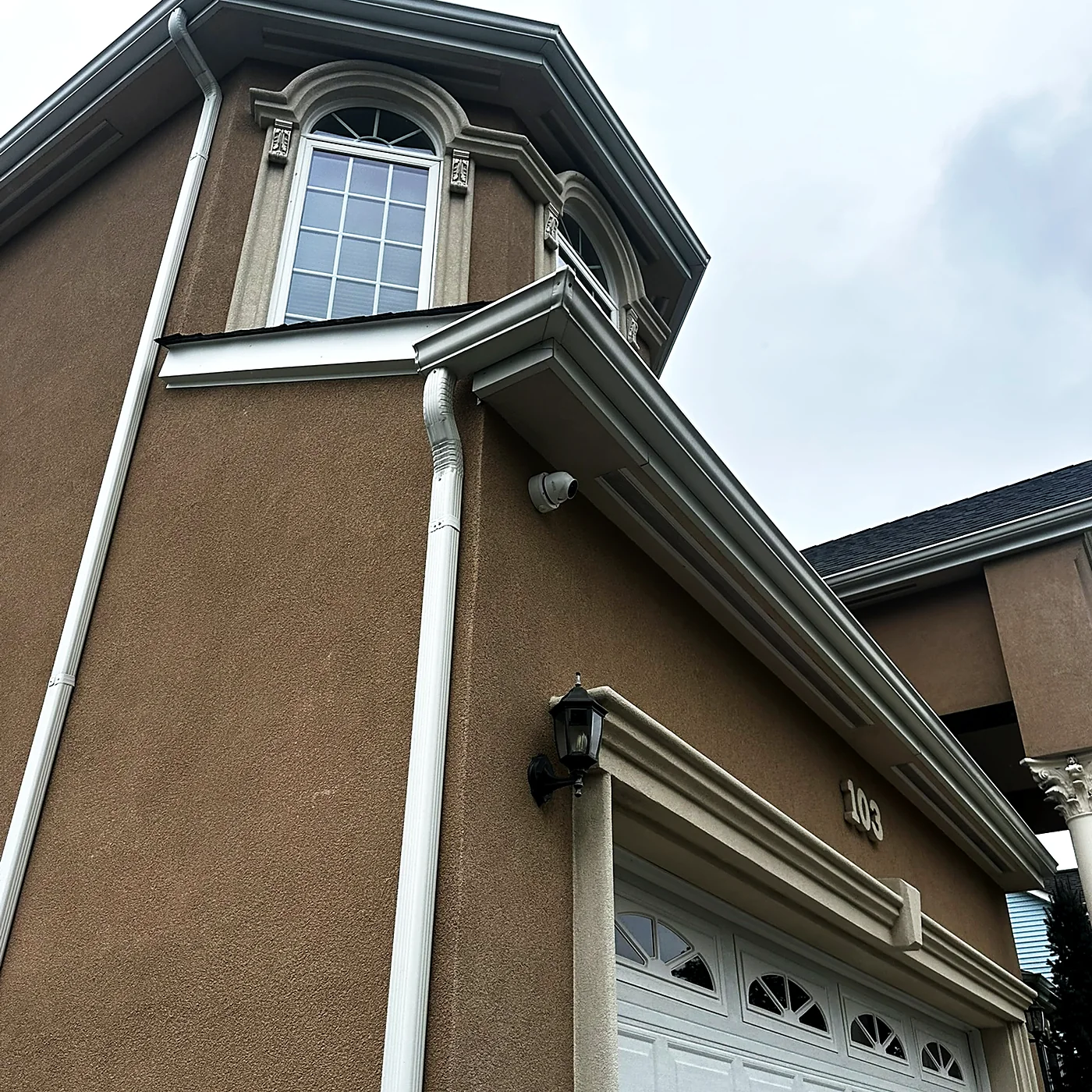 A camera mounted under the roofline of a stucco house, covering the garage door and driveway below.