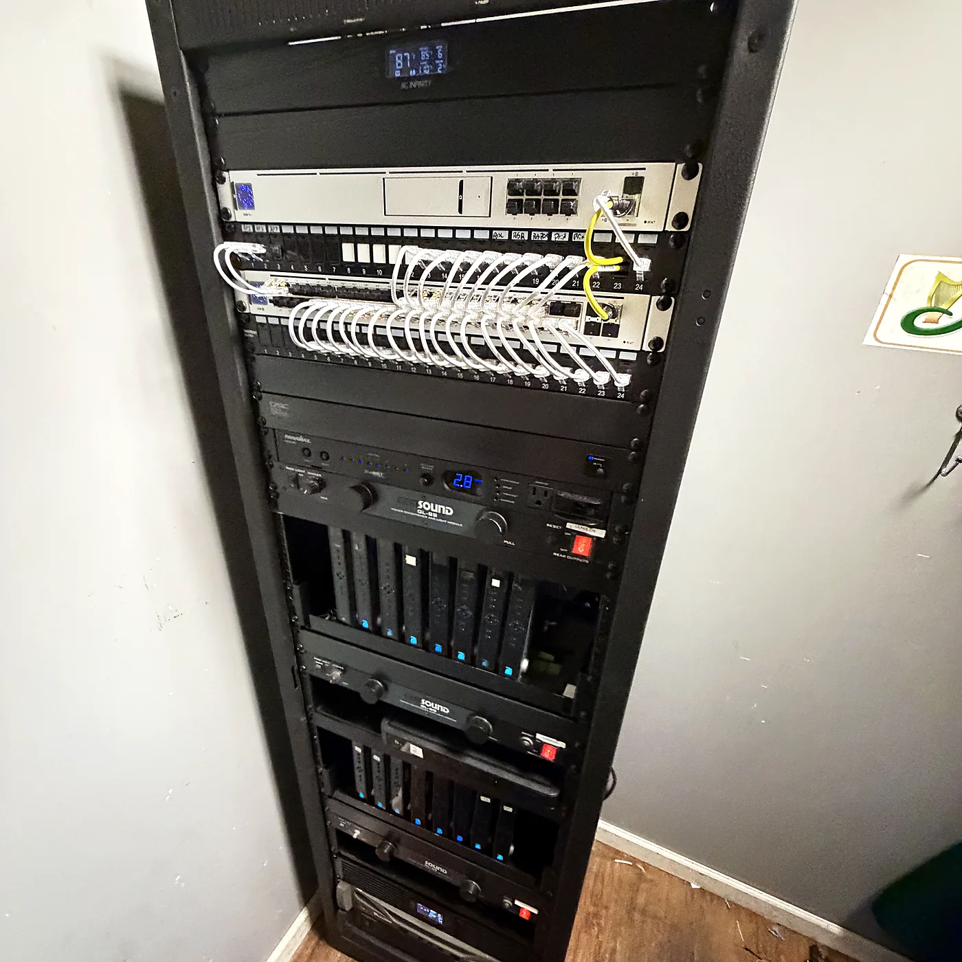 A floor-standing equipment rack with a white patch field routed through horizontal cable management, network and audio-visual equipment stacked below.