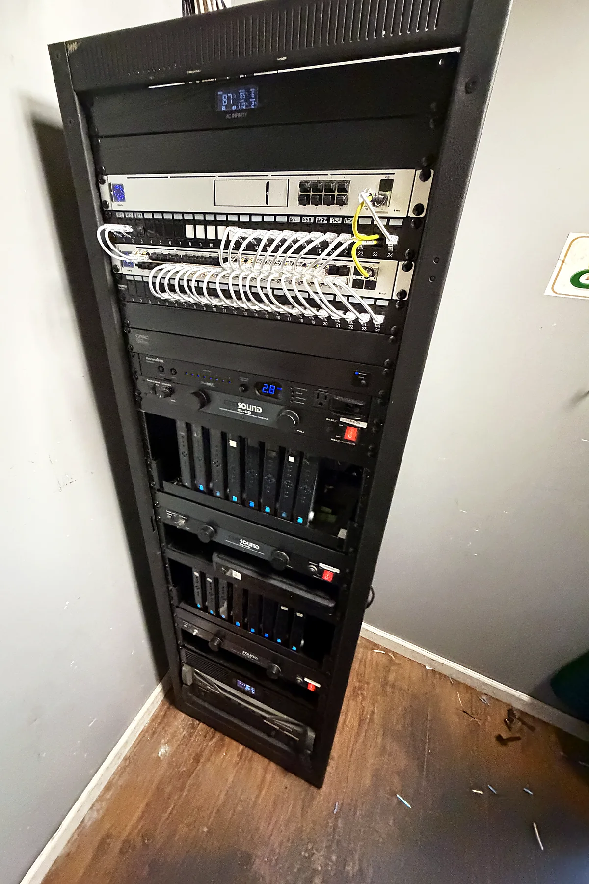A floor-standing equipment rack with a white patch field routed through horizontal cable management, network and audio-visual equipment stacked below.