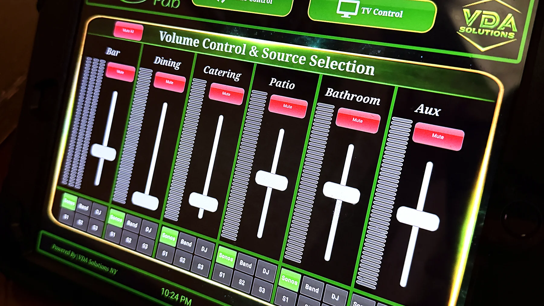 A wall-mounted touch panel showing a custom control interface with labelled volume faders for separate zones and a source selection row.