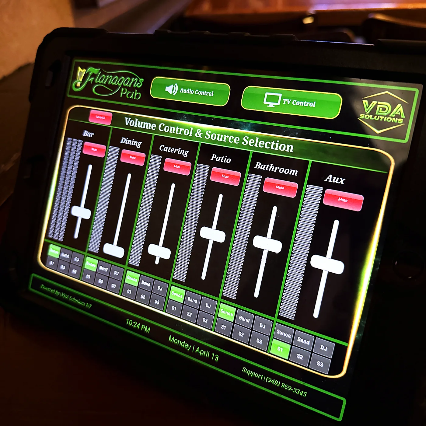 A wall-mounted touch panel showing a custom control interface with labelled volume faders for separate zones and a source selection row.