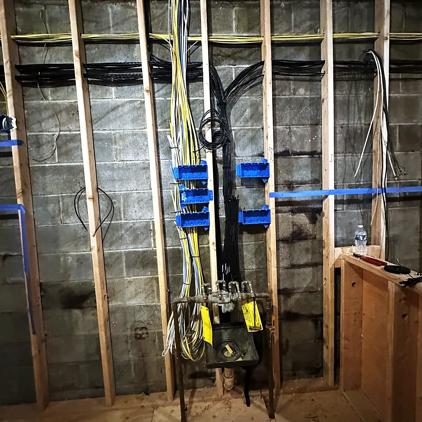 Cable bundles run vertically down a block wall between timber studs, supported on blue cable hangers, with a distribution point terminated at the base.
