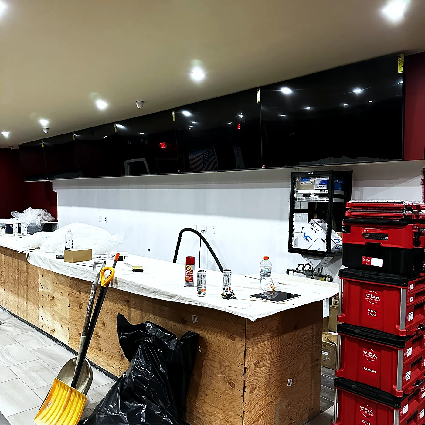 A bar under construction with a display mounted behind it and tool cases staged on the floor.