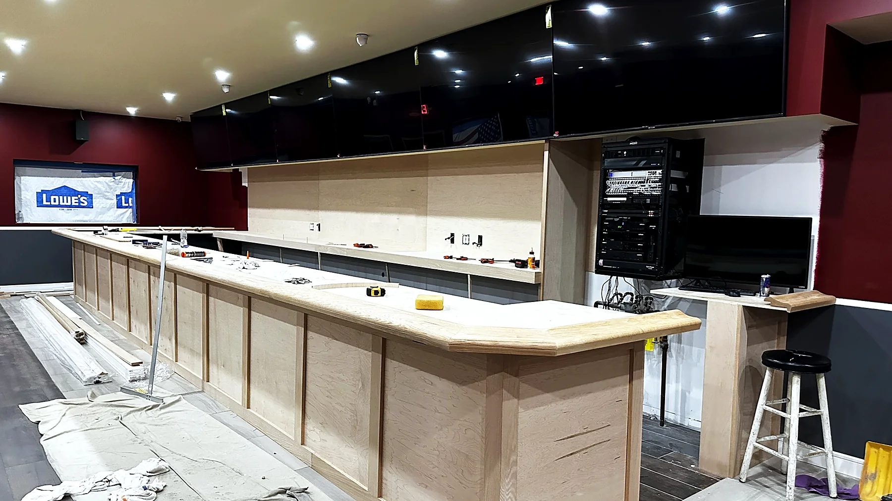 The same bar during installation — displays mounted but dark, drop cloths on the floor, millwork unfinished.