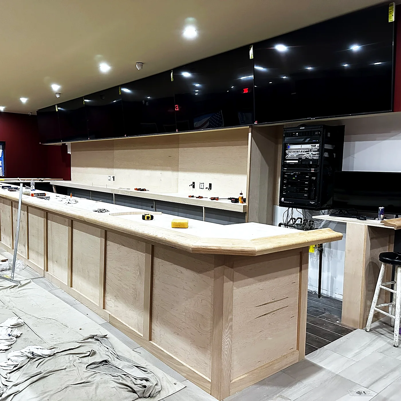 The same bar during installation — displays mounted but dark, drop cloths on the floor, millwork unfinished.