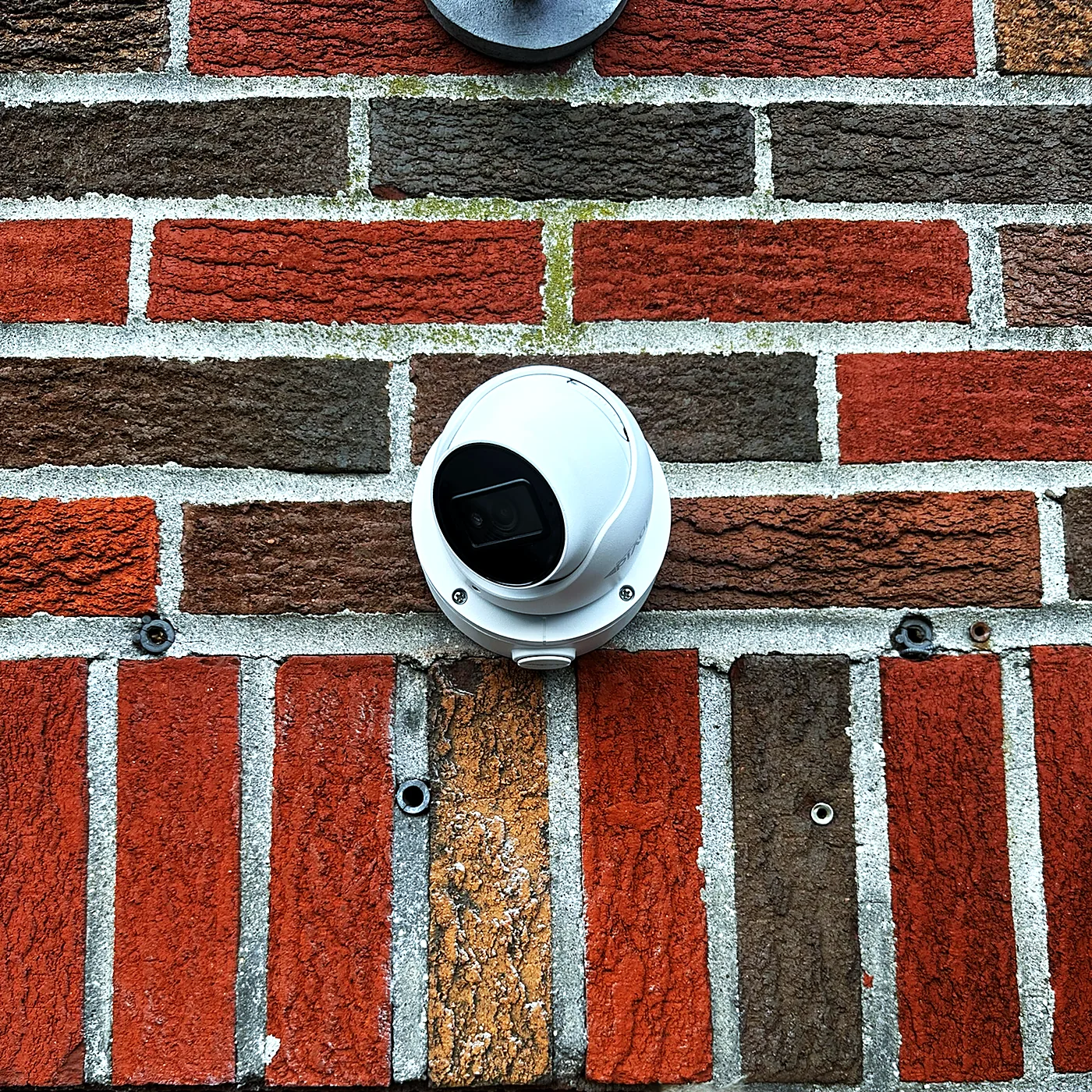 A white turret camera mounted on a multi-tone brick wall above a doorway.