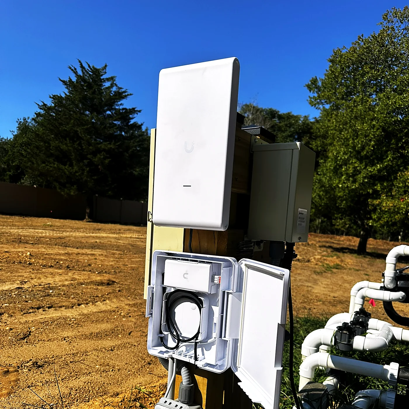 A point-to-point wireless bridge antenna and a weatherproof enclosure mounted on a post in an open field.