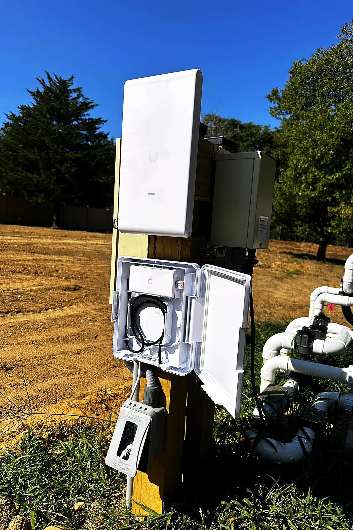 A point-to-point wireless bridge antenna and a weatherproof enclosure mounted on a post in an open field.